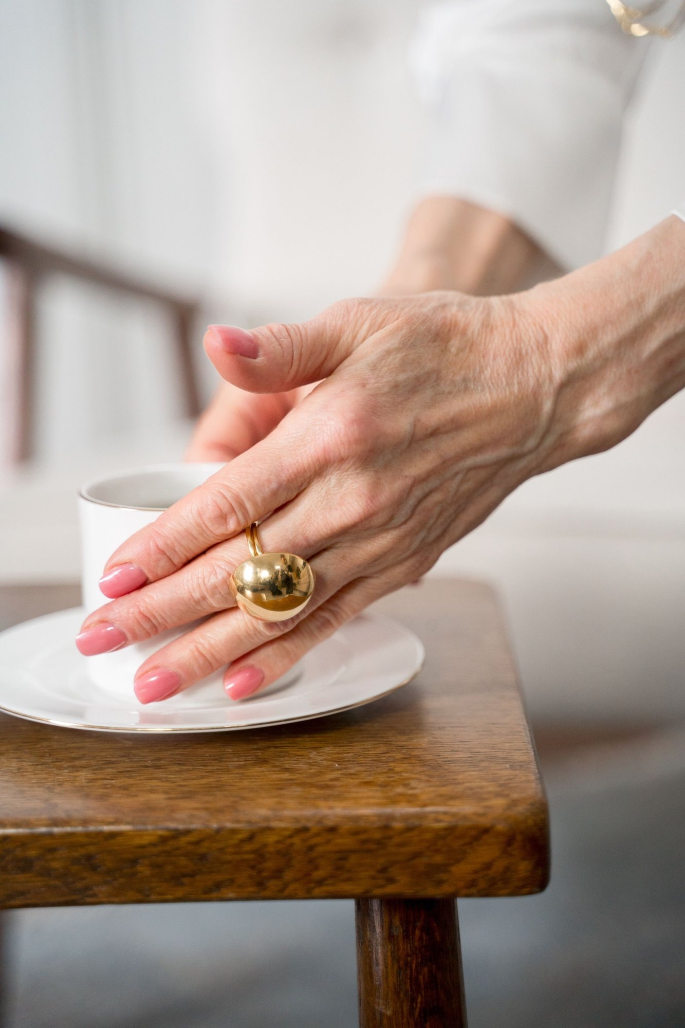 Una mano con un anello d’oro a sfera posata su una tazzina