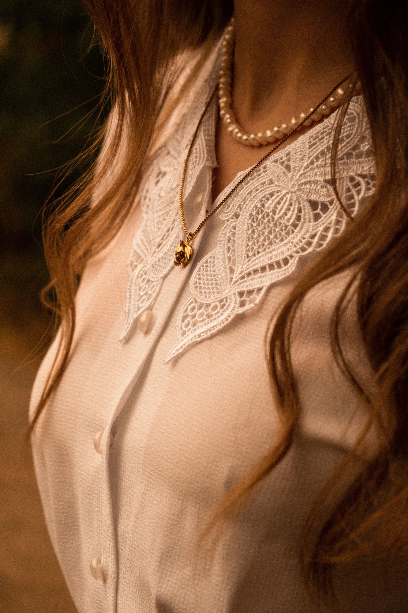 Una collana di perle con un pendente d’oro su una camicetta di pizzo